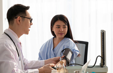 Obraz premium Young Male Doctor talking to his female patient. Doctor listening to a patient in his office. Speaking and Explaining with cheerful young patient while measuring blood pressure. 