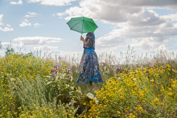 Woman in field of flowers holding umbrella, cloudy sky background