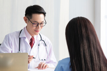 Charming male doctor giving advice to a female patient. Doctor working in the office and talking with his patient, healthcare and assistance concept. Young doctor consulting with patient. Covid-19.