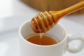 Honey dripping from wooden spoon into the Cup