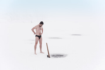 young man cuts ice with an ax on a lake