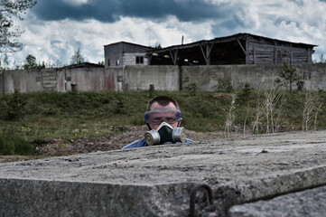 A man with a gas mask hid among the ruins and the dramatic background of the sky. Biohazard concept. Environmental pollution, ecological disaster, radiation