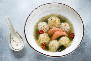 Panasian wonton and shrimp soup served in a white bowl over light-blue stone background, studio shot