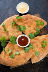 Sliced ossetian pie with fresh cilantro leaves and dipping sauces, vertical shot, close-up