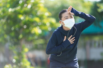 Portrait of Asian woman running at village park listening to music and wearing mask.