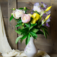 Bouquet of pink peonies and yellow irises in a vase on a wooden background. Still life for decoration. © IrinaBogach