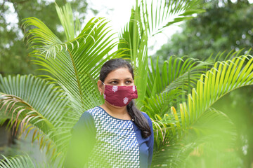 an indian lady is standing in garden with wearing face mask due to covid 19 pandemic