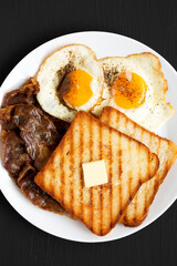Homemade Healthy Sunnyside Eggs Breakfast on a white plate on a black background, top view. Flat lay, overhead, from above.