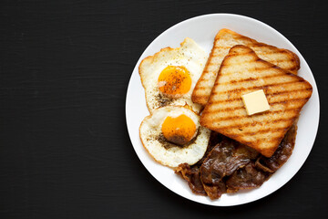 Homemade Healthy Sunnyside Eggs Breakfast on a white plate on a black surface, top view. Flat lay, overhead, from above. Copy space.