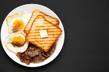 Homemade Healthy Sunnyside Eggs Breakfast on a white plate on a black surface, top view. Flat lay, overhead, from above. Space for text.