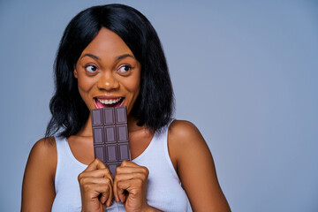 Close-up positive woman eating a dark chocolate bar and looking at the camera. Diet concept