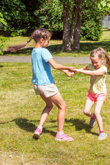 Fototapeta premium Dwie szczęśliwe małe siostry dziewczynki, trzymając się za ręce, bawić się w parku w słoneczny letni dzień.