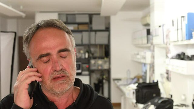 uomo cinquantenne cammina nel suo ufficio rivolto verso la finestra parlando animatamente al telefono
