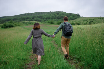 A man and a woman go hand in hand on a trodden path on a background of nature. The couple goes back.