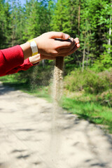 hands of a young boy with with pouring sand with the nature landscape on the background
