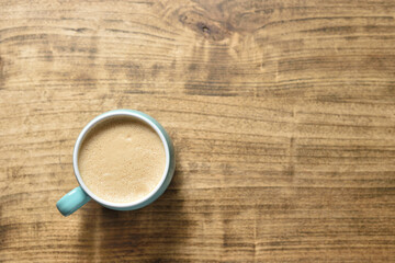 Coffee mug with foam and wooden table, top view and copy space