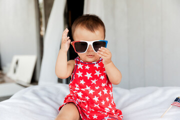 Patriotic baby girl wearing red dress and sunglasses on Independence Day on 4th of July