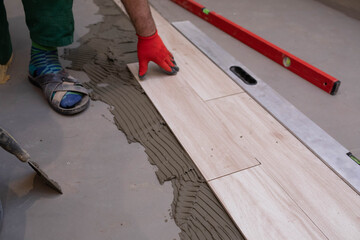 The builder presses the ceramic tile against the floor to align it with the previously laid tiles.