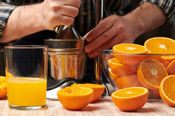 Squeezing an orange with a manual press, close view, making a glass of fresh. Fresh oranges on a wooden table, whole, squeezed and sliced.