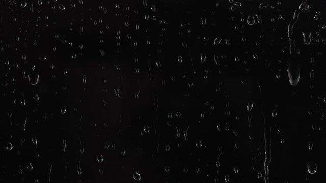 4K footage of rain drops falling on window glass on black background.