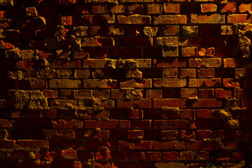 Old grungy and damaged red brick wall at night with light of a lantern shining on it