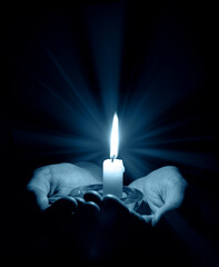 Hands holding a burning candle in dark room