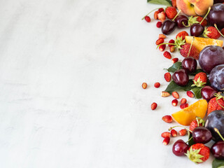 Various berries and fruits on a white background. Border of strawberries, wild strawberies, cherries, peach, plum. Copy space