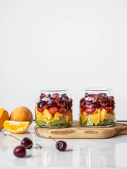 Two glass jars with berries and fruits. Fruit salad with kiwi, peach, strawberry, cherries and plum in glass jars on wood board. Summer seasonal tasty vegetarian salad for a snack or lunch