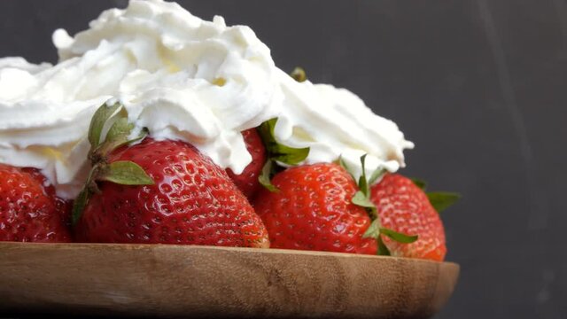 Juicy ripe big red strawberries on an eco bamboo plate on top with whipped cream cloes up view.