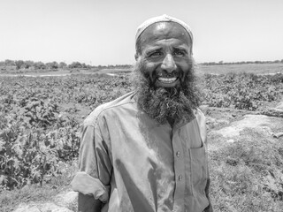 a pakistani farmer with beard working in vegetable fields and smiling
