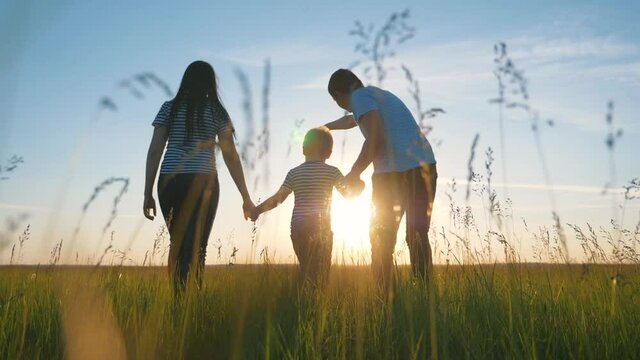 Happy family. Mom dad and son in an outdoor team walk through a green meadow at sunset. Healthy, active lifestyle of a married couple. Parents with a child have fun.