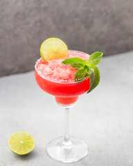 Watermelon margarita cocktail with lime. Watermelon summer cocktail with ice and mint leaves. Cold refreshment drink in a glass with water drops. Low depth of field, selective focus.