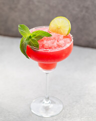 Watermelon margarita cocktail with lime. Watermelon summer cocktail with ice and mint leaves. Cold refreshment drink in a glass with water drops. Low depth of field, selective focus.