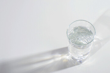 Glass glass with clean water on a light background with hard light and reflection. Distorted glass water