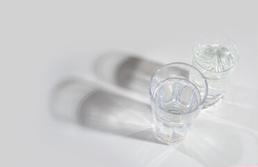 Glass glass with clean water on a light background with hard light and reflection. Distorted glass water