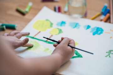 child's hand drawing clouds with a watercolour brush at home