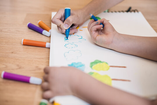 child's hand and woman's hand drawing clouds with colored markers at home