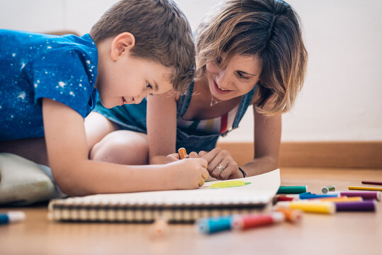 child drawing with young woman with colored markers at home