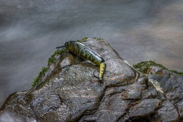 Colorful fishing hook, plummet and baits for catching fish on wet rock background. Long exposure of silky smooth water. Fishing and hobbies concepts, close up