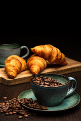 Cup with coffee beans on a black background. Freshly roasted arabica. Several fresh croissants on a wooden board.