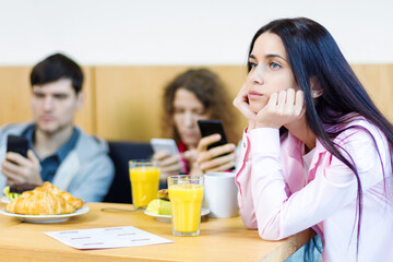 Young people guys and girls are having meeting, sitting at table in cafe. Friends are holding smartphones and browsing social networks instead of speaking. Addiction to gadgets, internet concept.