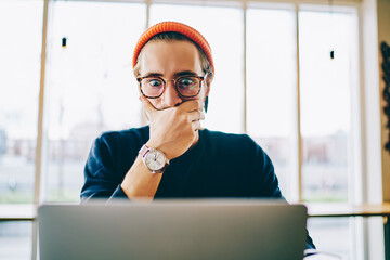 Shocked young hipster guy in spectacles amazed with good 4G connection watching movie online on...