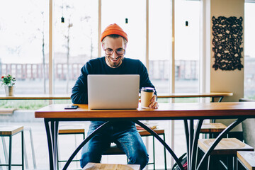 Positive caucasian male freelancer satisfied with chatting online on laptop computer on coffee...