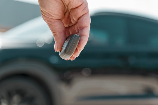 close-up woman hand presses a button on the car remote control against blur black car.