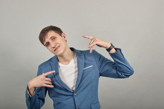 Giving rock and roll sign, showing symbol of the horns, language gestures with fingers. Young attractive man, dressed blue jacket, grey background