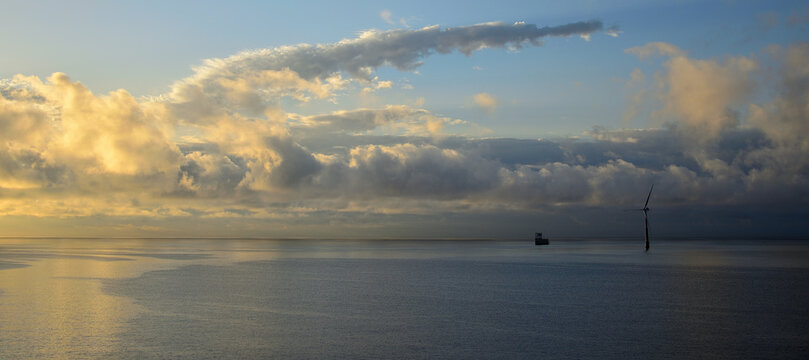 Sunrise seen from the coast with calm sea, cloudy sky and marine wind turbine