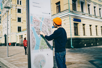 Young male traveler using modern smart board with map and useful information for tourists, back...
