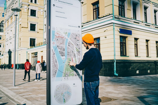 Fototapeta Young male traveler using modern smart board with map and useful information for tourists, caucasian hipster guy searching train on electronic device on street with wifi connection and touchscreen .