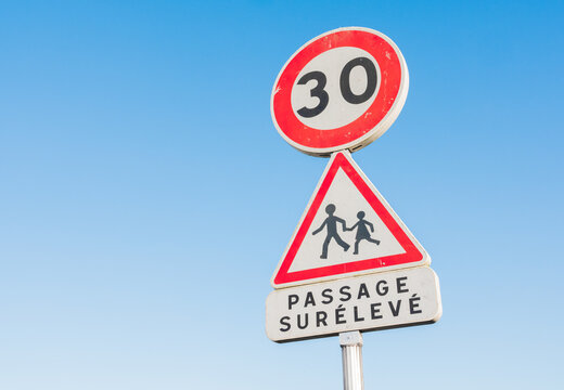 Round 30 kilometers per hour speed limit road sign in a children school area. Written in french "passage sur&eacute;lev&eacute;" (speedbump) Caution. Blue sky in the background.