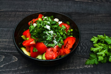 Fresh vegetables salad from tomatoes and cucumbers in black bowl on black wooden background. Healthy food concept. 
